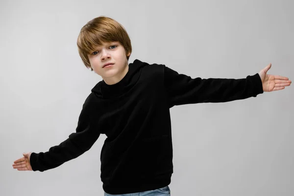 Ein hübscher Teenager in schwarzem Pullover und heller Jeans. der Junge breitete seine Hände in beide Richtungen aus — Stockfoto