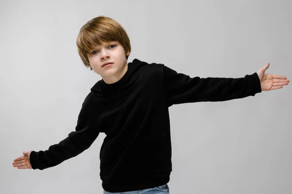 Een mooie tiener in een zwarte trui en lichte jeans. De jongen verspreid zijn handen in beide richtingen — Stockfoto