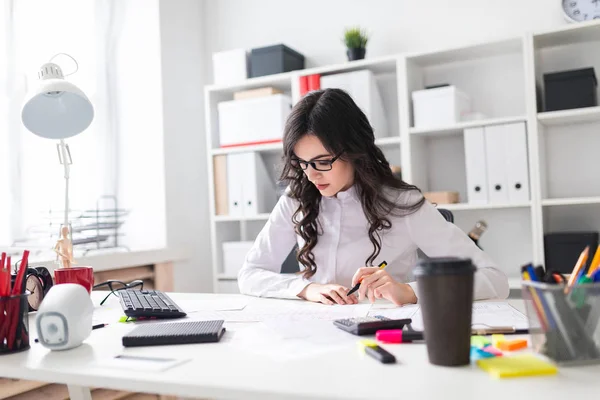 Een jong meisje zit aan de tafel van office, houdt een pen in haar hand en kijkt naar de documenten. — Stockfoto