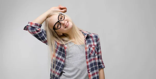 Hermosa chica adolescente con el pelo largo y con gafas. Una adolescente con una camisa a cuadros y una camiseta gris. Una adolescente puso su mano detrás de su cabeza . — Foto de Stock