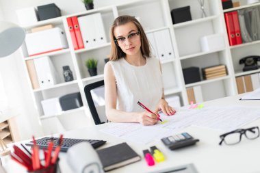 Güzel genç kız ofiste masada oturmuş, elinde kalem tutan ve belgeleri doldurma.
