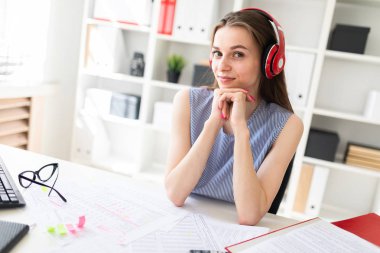 Güzel genç kız ofiste kırmızı kulaklıklar bir masada oturur.