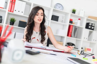 Güzel bir genç kız onun elinde belgeler ve bir kalem ile office masada oturuyor ve müzakere.