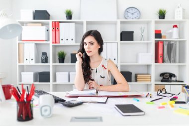 Güzel bir genç kız ofis masada oturur, saçları onun elinde tutan ve düz görünüyor.