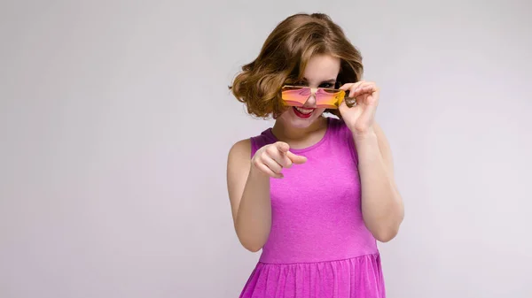 Charmante junge Mädchen in rosa Kleid auf grauem Hintergrund. fröhliches Mädchen mit quadratischer Brille. — Stockfoto