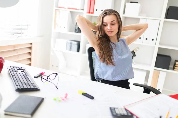 Menina bonita no escritório senta-se à mesa, colocando as mãos atrás da cabeça . — Fotografia de Stock