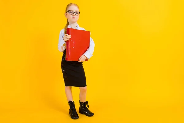 Menina com cabelo vermelho em um fundo amarelo. Uma garota encantadora em óculos transparentes está segurando uma grande pasta vermelha em suas mãos . — Fotografia de Stock