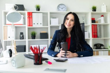 Güzel bir genç kız bir bardak kahve tablo ofiste bir sandalyede oturup ile düzenliyor.