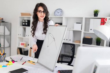 Güzel bir genç kız bir Ofis Masası standları ve manyetik bir işaretleyici manyetik tahtaya çizer.