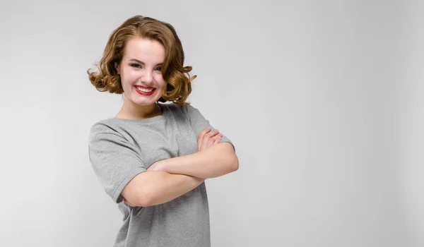 Charmantes junges Mädchen in einem grauen T-Shirt vor grauem Hintergrund. das Mädchen verschränkte die Arme über der Brust — Stockfoto