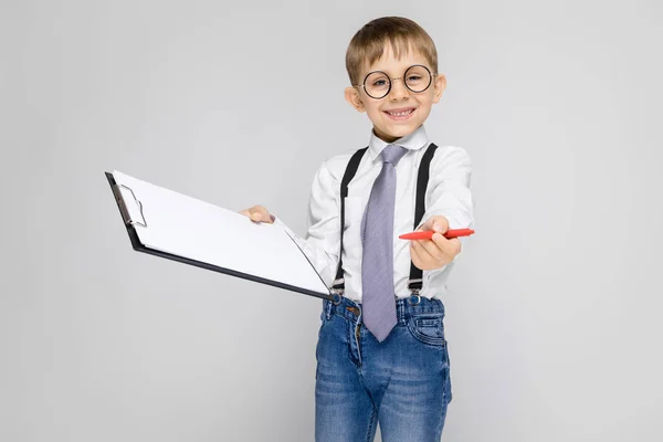 ペンとドキュメントを保持している灰色の背景の上に立って小さな男の子の肖像画 — ストック写真