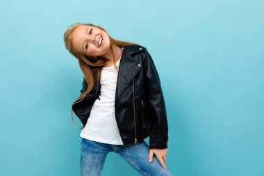 Siyah deri ceketli küçük havalı kız mavi arka plana poz veriyor. 
