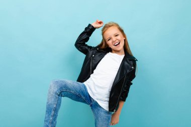 Siyah deri ceketli küçük havalı kız mavi arka plana poz veriyor. 