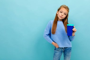Küçük şirin kız mavi arka planda kağıt bardakla poz veriyor. 