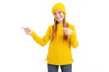 Sarı kazaklı ve şapkalı tatlı genç kız beyaz arka planda poz veriyor.  