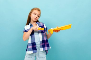 Küçük kız mavi arka planda boya silindiri ve yalakla poz veriyor. 