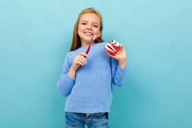 Mavi arka planda diş fırçasıyla poz veren küçük kız 