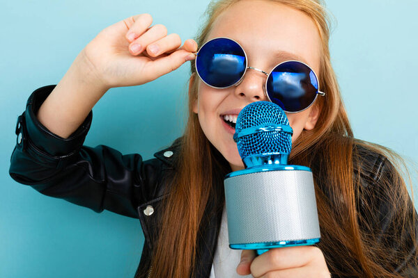 милая маленькая девочка в черной кожаной куртке позирует с микрофоном на синем фоне
 
