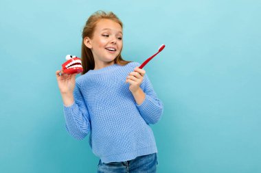 Mavi arka planda diş fırçasıyla poz veren küçük kız 