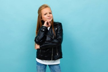 Siyah deri ceketli küçük havalı kız mavi arka plana poz veriyor. 