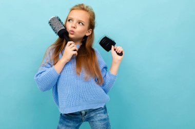 little girl posing with two hairbrushes against blue background 
