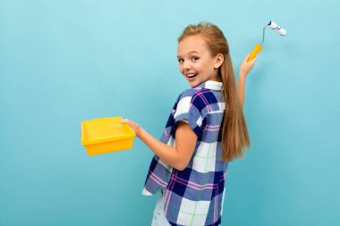 Küçük kız mavi arka planda boya silindiri ve yalakla poz veriyor. 