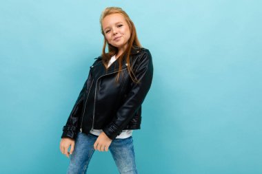 Siyah deri ceketli küçük havalı kız mavi arka plana poz veriyor. 