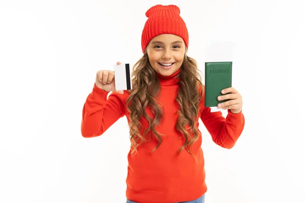 かわいい赤いセーターの女の子と白い背景にパスポートとクレジットカードでポーズをとる帽子 — ストック写真