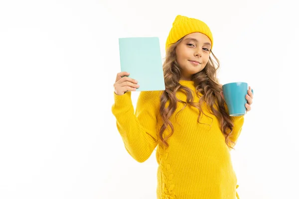 cute little girl in yellow clothes posing with book and mug against white background