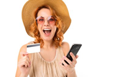 Genç bir kadın cep telefonu ve kredi kartıyla beyaz arka planda poz veriyor.  
