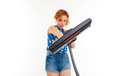 Genç kızıl saçlı kadın elektrik süpürgesi beyaz arka planda poz veriyor.  