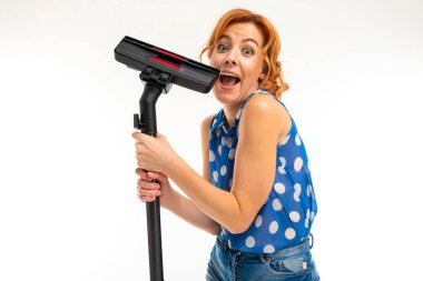Genç kızıl saçlı kadın elektrik süpürgesi beyaz arka planda poz veriyor.  