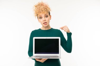 Beyaz arka planda dizüstü bilgisayarla poz veren yeşil elbiseli genç kadın.  