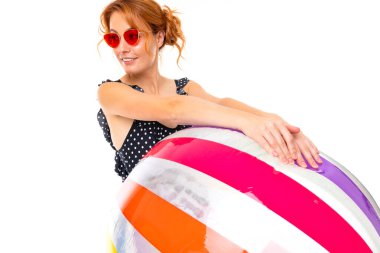 Güneş gözlüklü genç kadın beyaz arka planda şişme topla poz veriyor.  