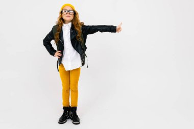 Lazer ceketli havalı küçük kız, arka planda sırt çantasıyla stüdyoda poz veriyor. 