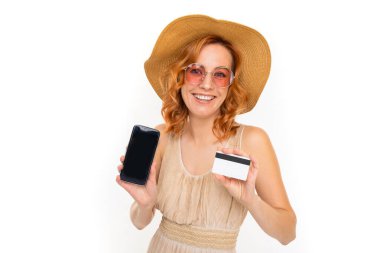 Genç bir kadın cep telefonu ve kredi kartıyla beyaz arka planda poz veriyor.  