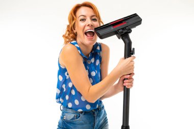 Genç kızıl saçlı kadın elektrik süpürgesi beyaz arka planda poz veriyor.  