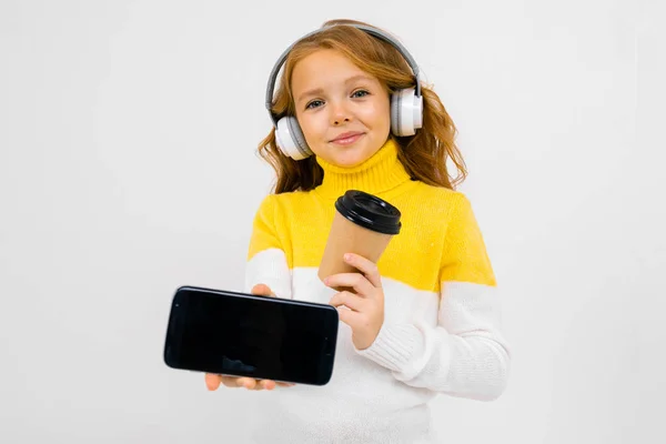 Cute Little Girl Słuchawki Pozowanie Papierowym Kubkiem Telefon Komórkowy Studio — Zdjęcie stockowe