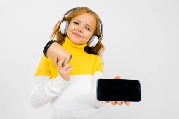 Cute Little Girl Słuchawki Pozowanie Papierowym Kubkiem Telefon Komórkowy Studio — Zdjęcie stockowe