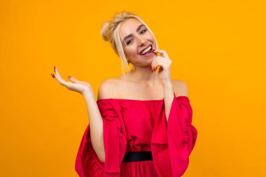 Sarı stüdyo arka planında elini tutan kırmızı elbiseli çekici sarışın kız.