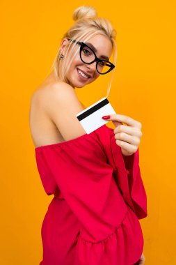 Kırmızı şık elbiseli Avrupalı bir kız. Kredi kartıyla sarı stüdyo arka planında bir model almış.