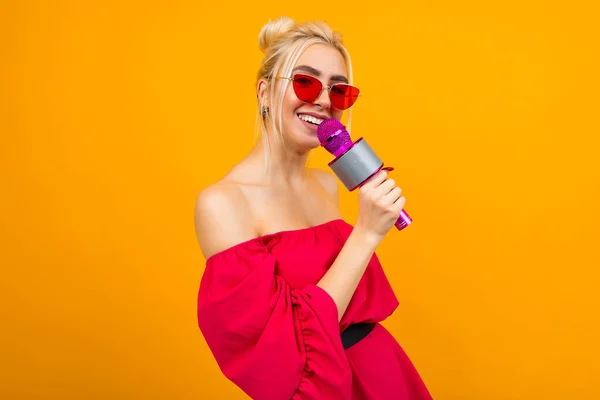 European blond girl singer in a bright red dress with manicure with a microphone in her hands on a yellow studio background — стокове фото