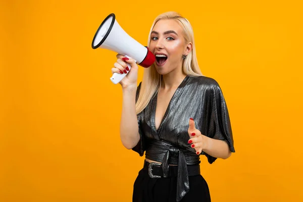 attractive girl in a blouse shouting news in a megaphone on a yellow studio background