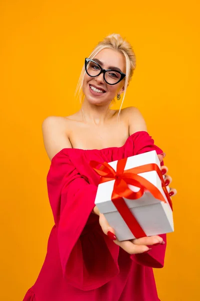 Meglepett vonzó lány piros ruhában tart egy ajándékot az ünnep egy narancs háttér — Stock Fotó