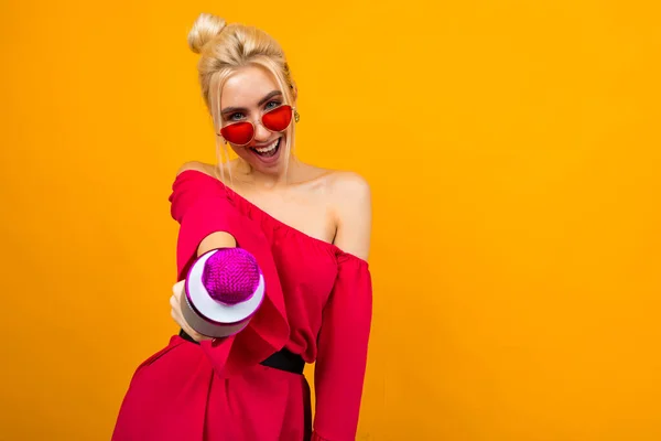 Europeisk sexig flicka sångare i en ljus röd klänning med bara axlar med en mikrofon i händerna på en gul bakgrund — Stockfoto