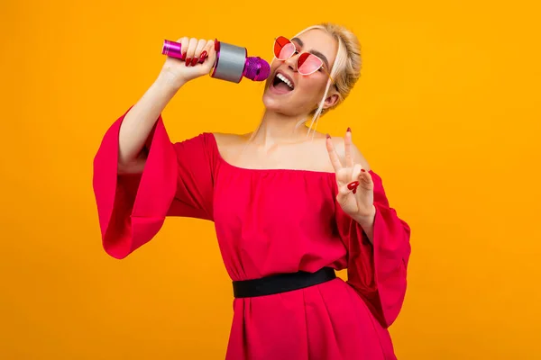 Europea sexy chica en un vestido rojo con hombros desnudos canta con un micrófono en el estudio — Foto de Stock