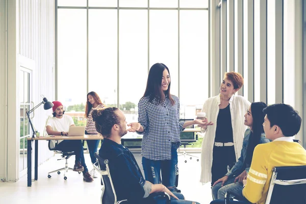 Modern ofiste konuşan, gülen ve beyin fırtınası yapan çok ırklı genç bir grup. 