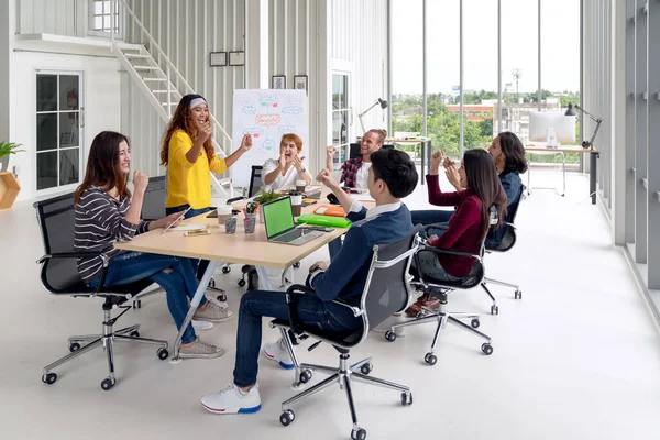 Modern ofiste konuşan, gülen ve beyin fırtınası yapan çok ırklı genç bir grup. 