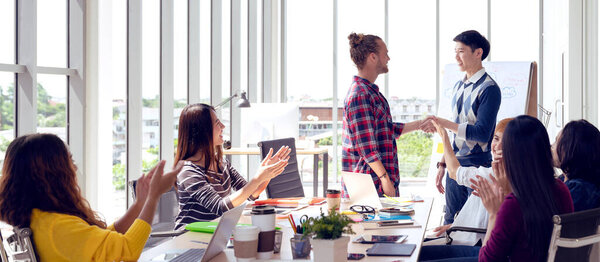 Young creative design asian team happy warm welcome with cheerful to new cowork employee in meeting or training at office. Happy asian workplace in small business or startup in millennials concept.