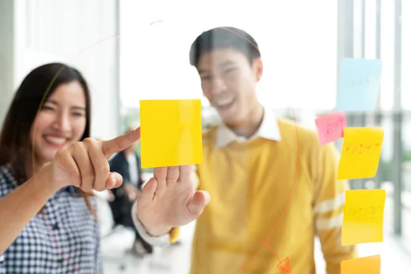 Genç ve başarılı yaratıcı erkek ve kadın bürodaki projede gülümseyip beyin fırtınası yaparak sarı notayı ya da yapışkan notu işaret ediyorlar. Yakın plan çift cam duvar konsepti fikrini paylaşıyor.